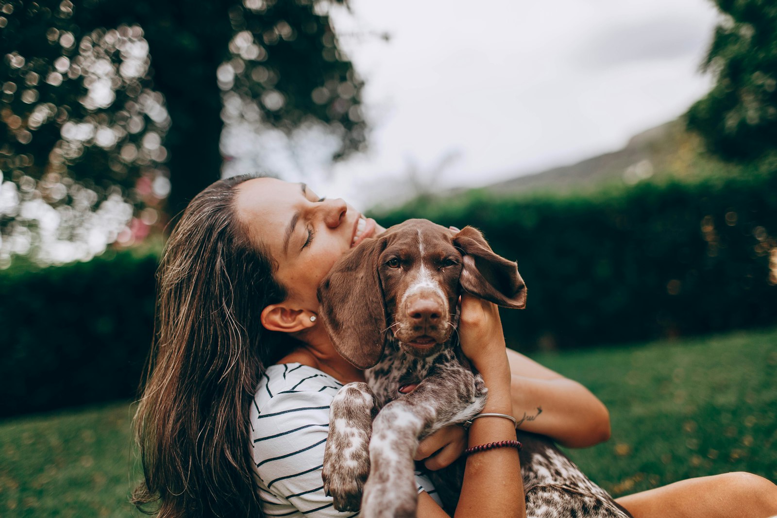 A smiling woman hugging her brown and white puppy in a garden